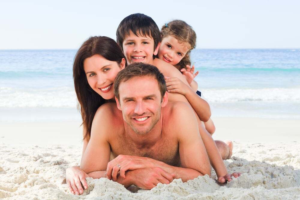 family on a beach with the mother and kids on top of their father and husband